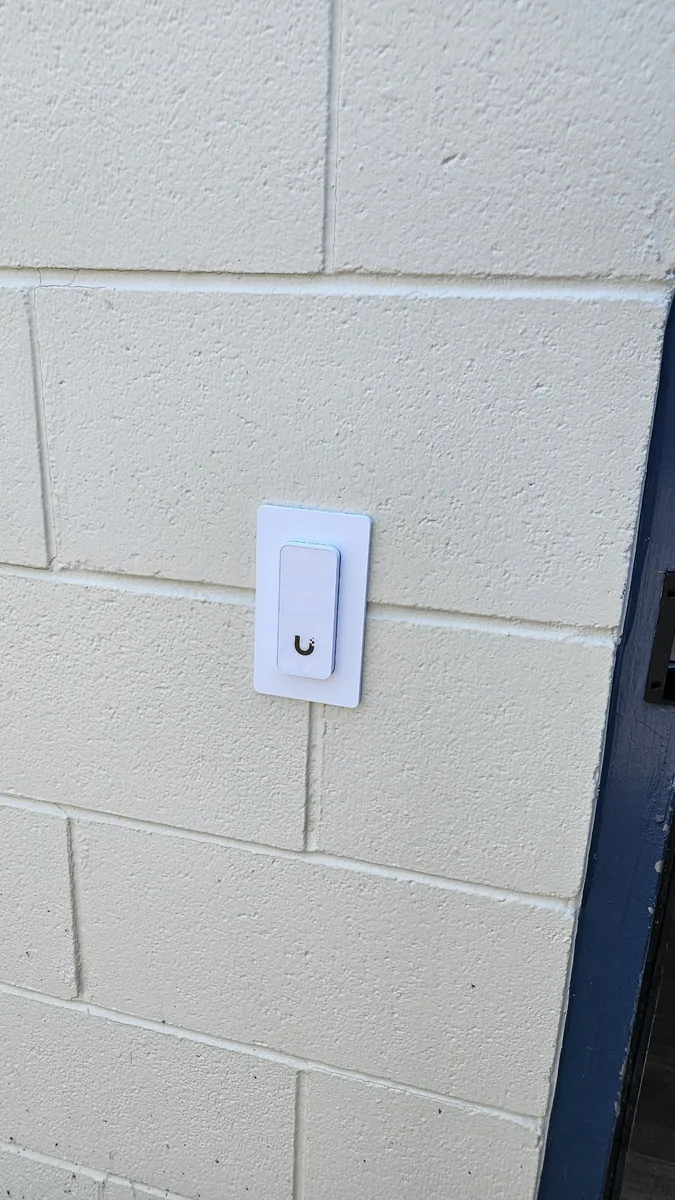 A Ubiquiti access control reader installed by KeenAI on an exterior block wall beside a door