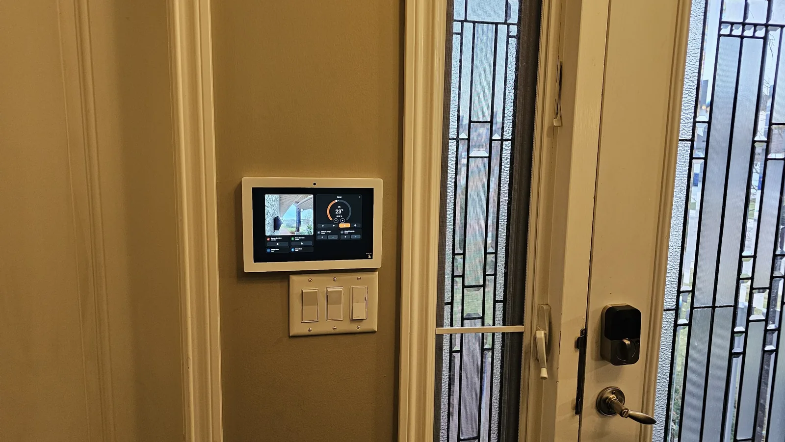 Wall-mounted control panel at a home entry with a smart deadbolt on the door alongside