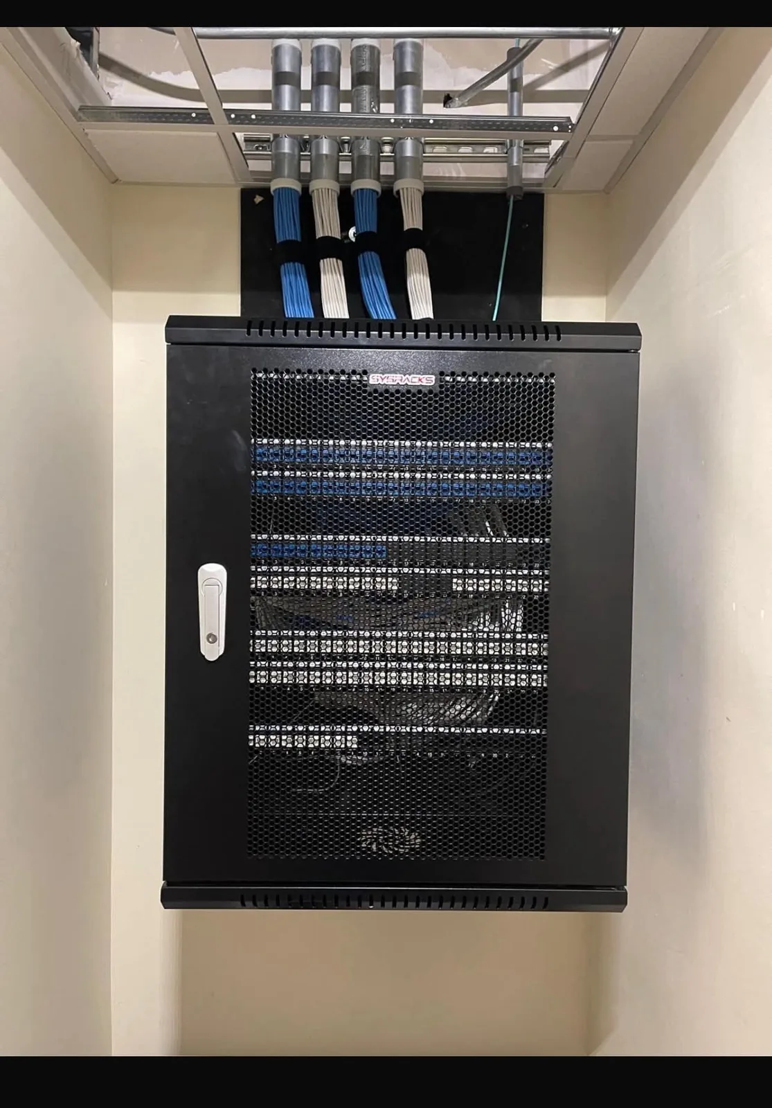 A wall-mounted equipment rack installed by KeenAI, closed and tidy, with cabling entering through conduit