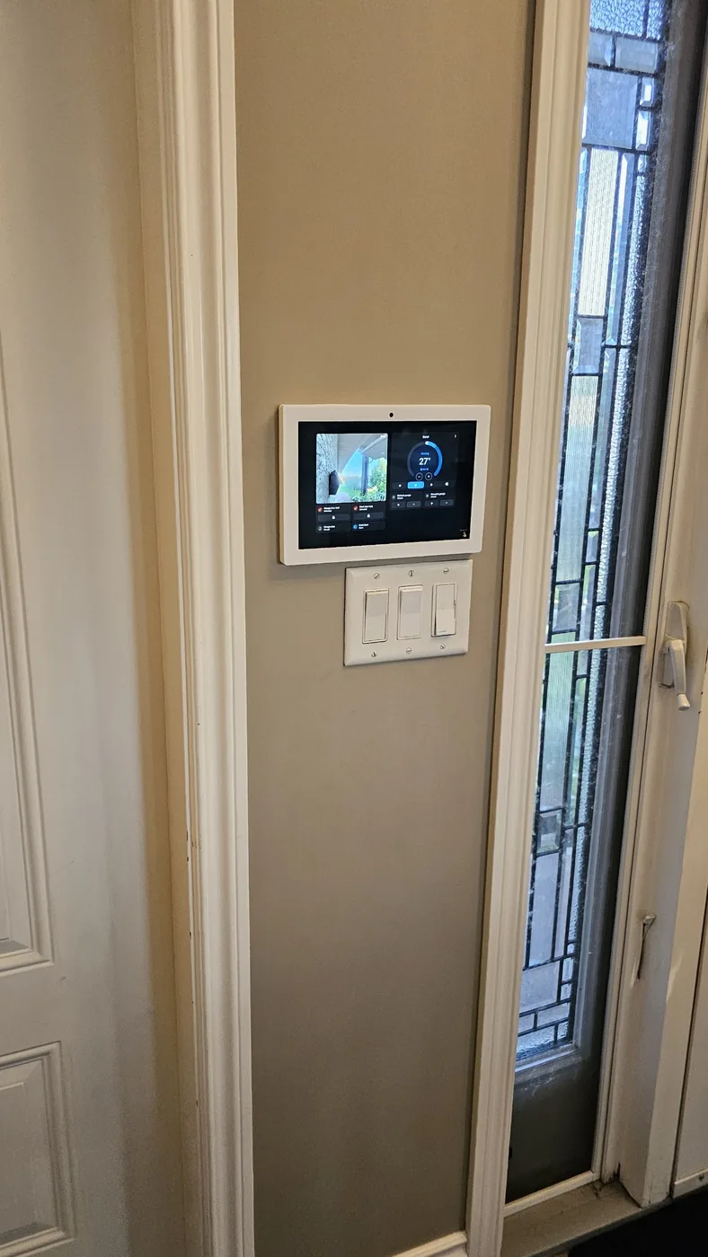 A wall-mounted touchscreen installed by KeenAI showing the current indoor temperature alongside camera and door status